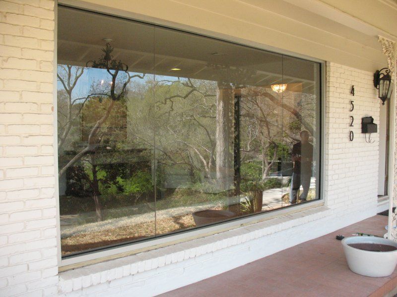A large, rectangular glass window framed in white brick, reflecting a porch and trees on a house with the number 4520.