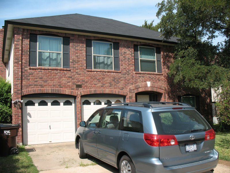 A two-story brick house with a two-car garage and a gray minivan parked in the driveway.