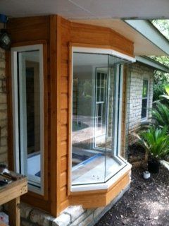 A newly installed wooden bay window unit set into a brick exterior wall, partially covered by an overhanging roof.