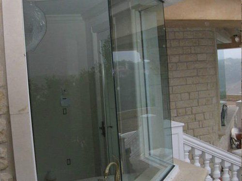 A glass shower enclosure with a gold faucet, set against a stone-walled interior with a view of an outdoor staircase.