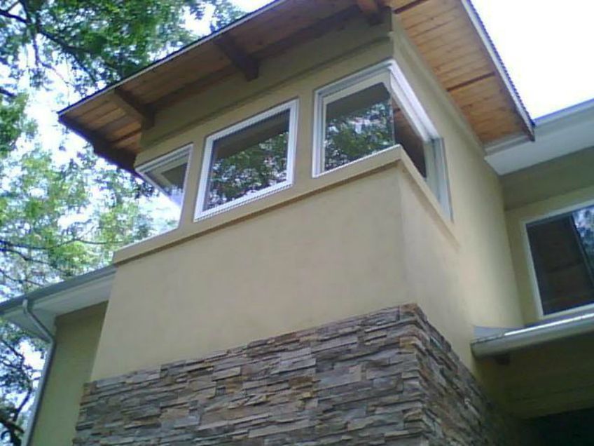 Tan stucco home exterior featuring a stone-clad base, corner windows, and a wood-paneled eave under the roofline.