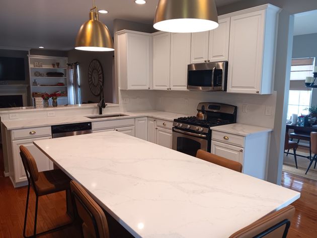 Modern kitchen with white cabinets, marble island, gold pendant lights, and stainless steel appliances.