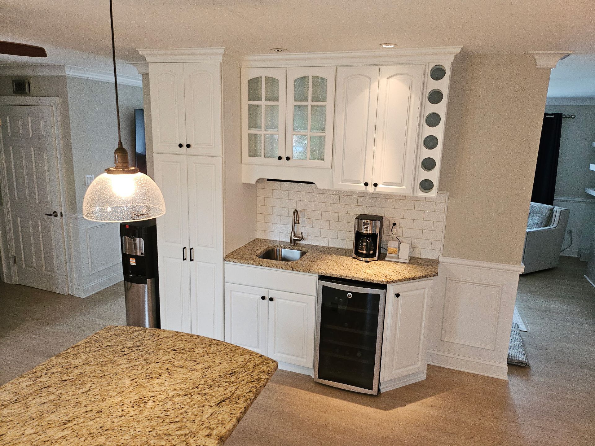 Bright kitchen with white cabinets, granite island, pendant light, and built-in wine rack