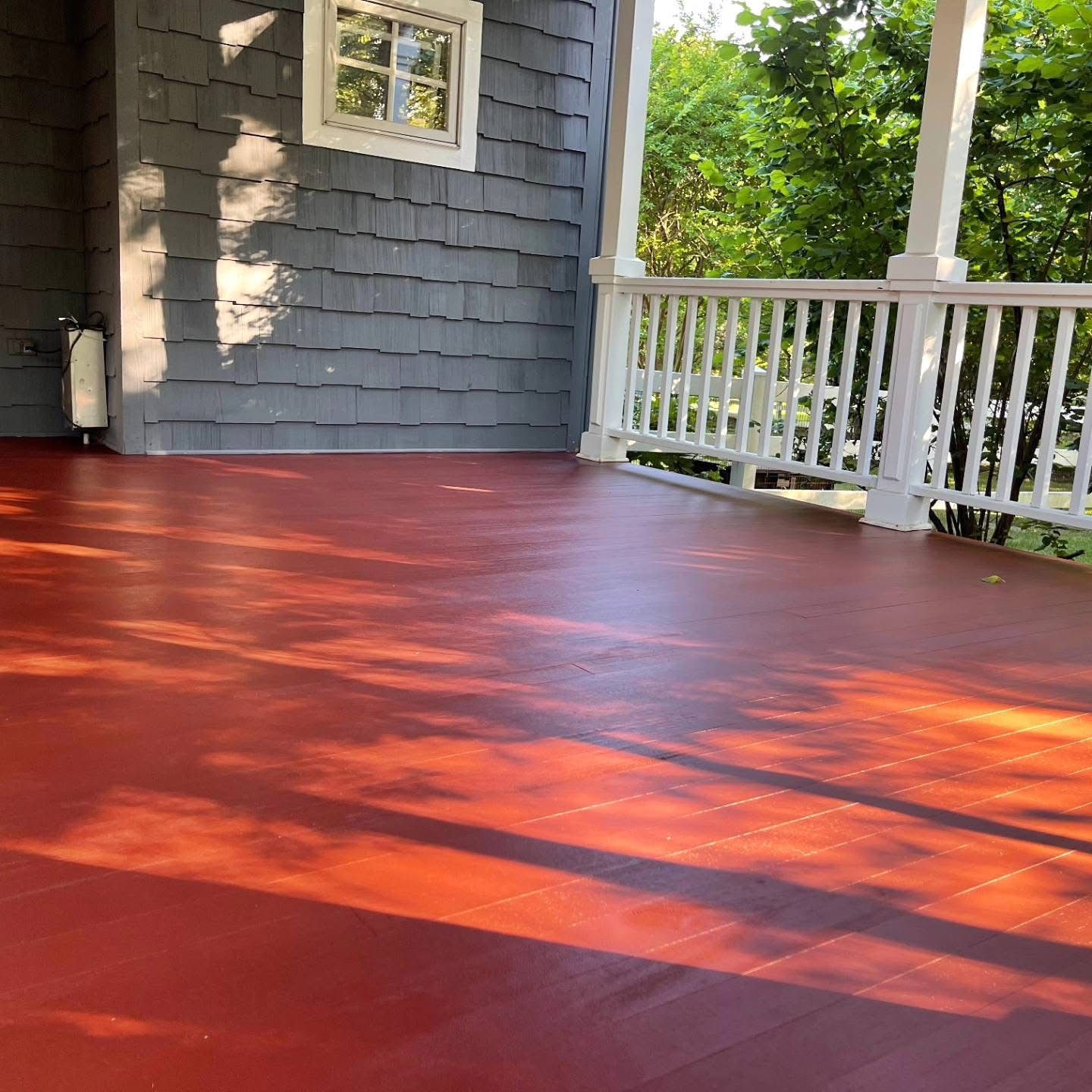 Red-painted wooden porch deck with white railing and gray house siding in sunlight
