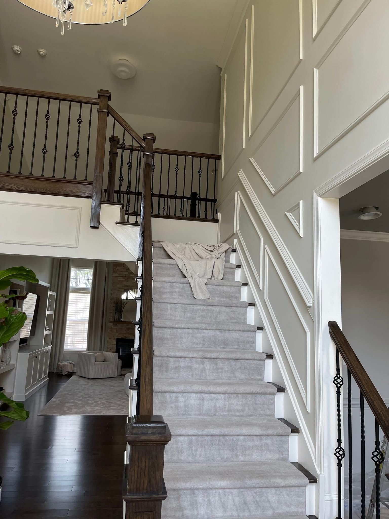 Staircase in a bright foyer with white walls, gray carpet, and dark wood railing leading to an upstairs landing