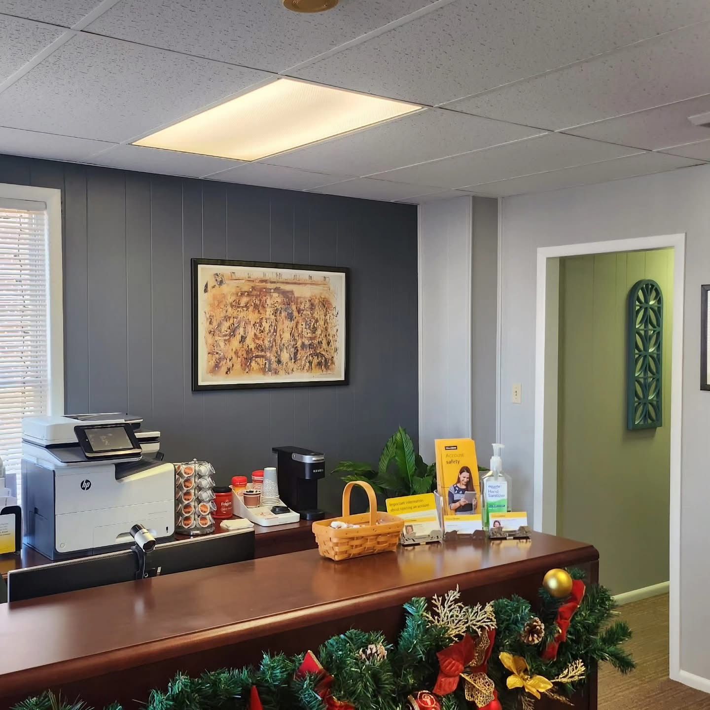 Office reception desk with coffee machine, basket, and holiday garland in a gray-walled lobby