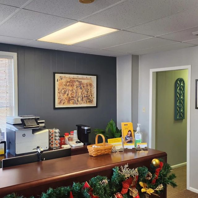 Small office reception desk with holiday garland, printer, coffee station, and framed art on gray walls.