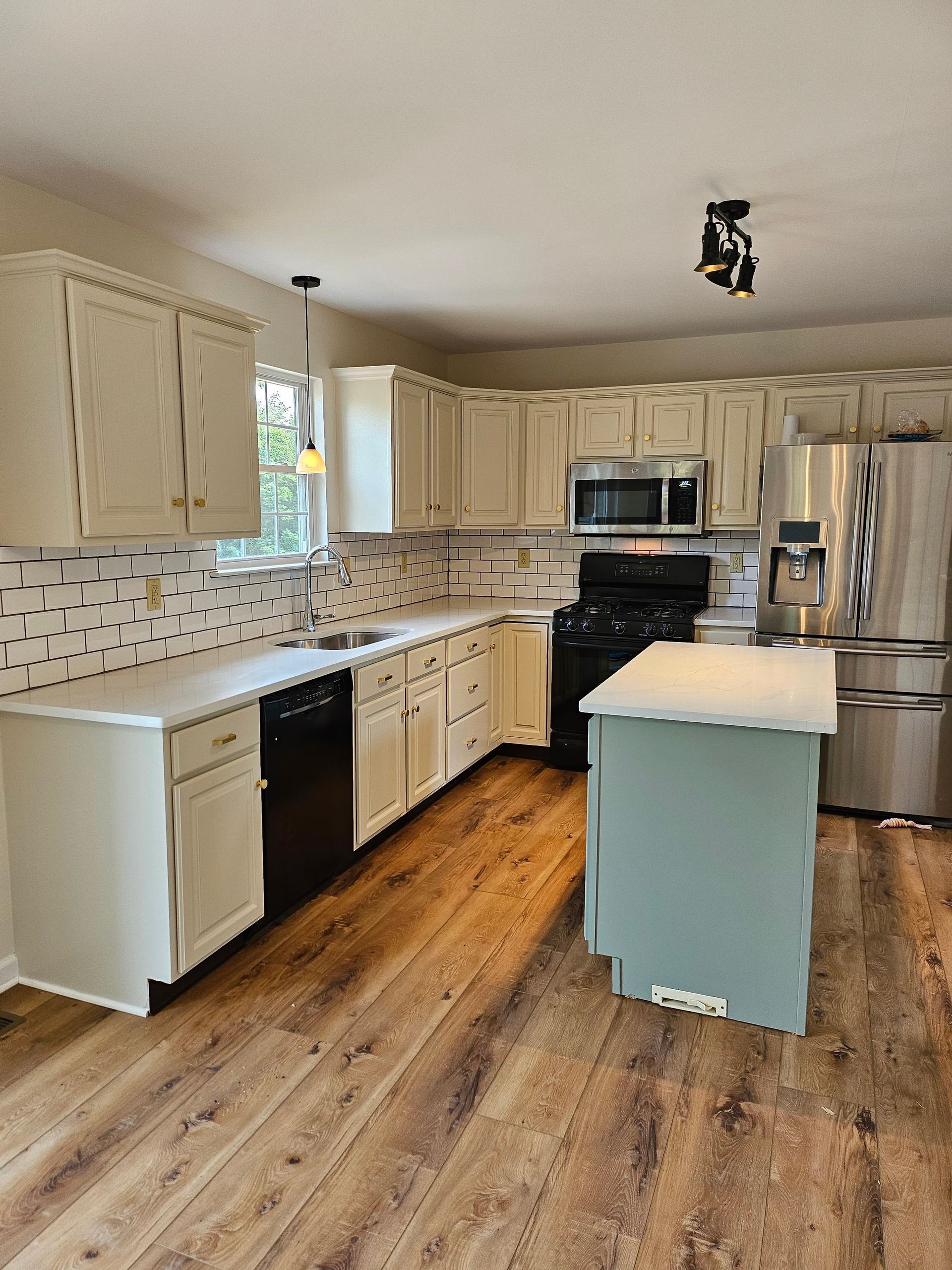 Bright kitchen with cream cabinets, stainless appliances, wood floors, and a small island.