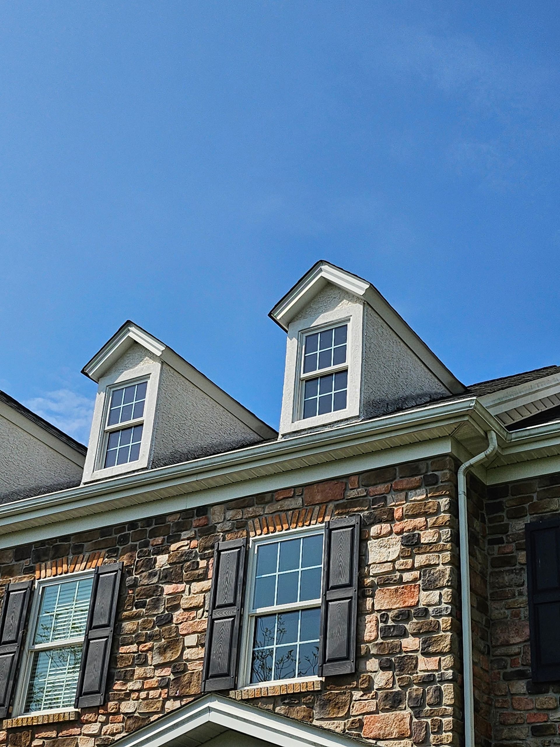Stone house exterior with white dormer windows under a clear blue sky