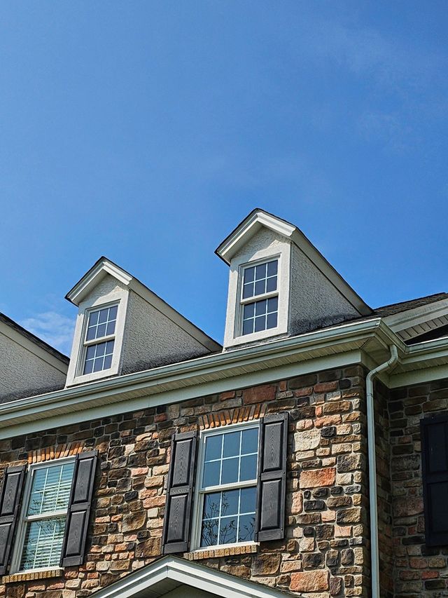 Stone house facade with blue shutters and dormer windows against a clear blue sky