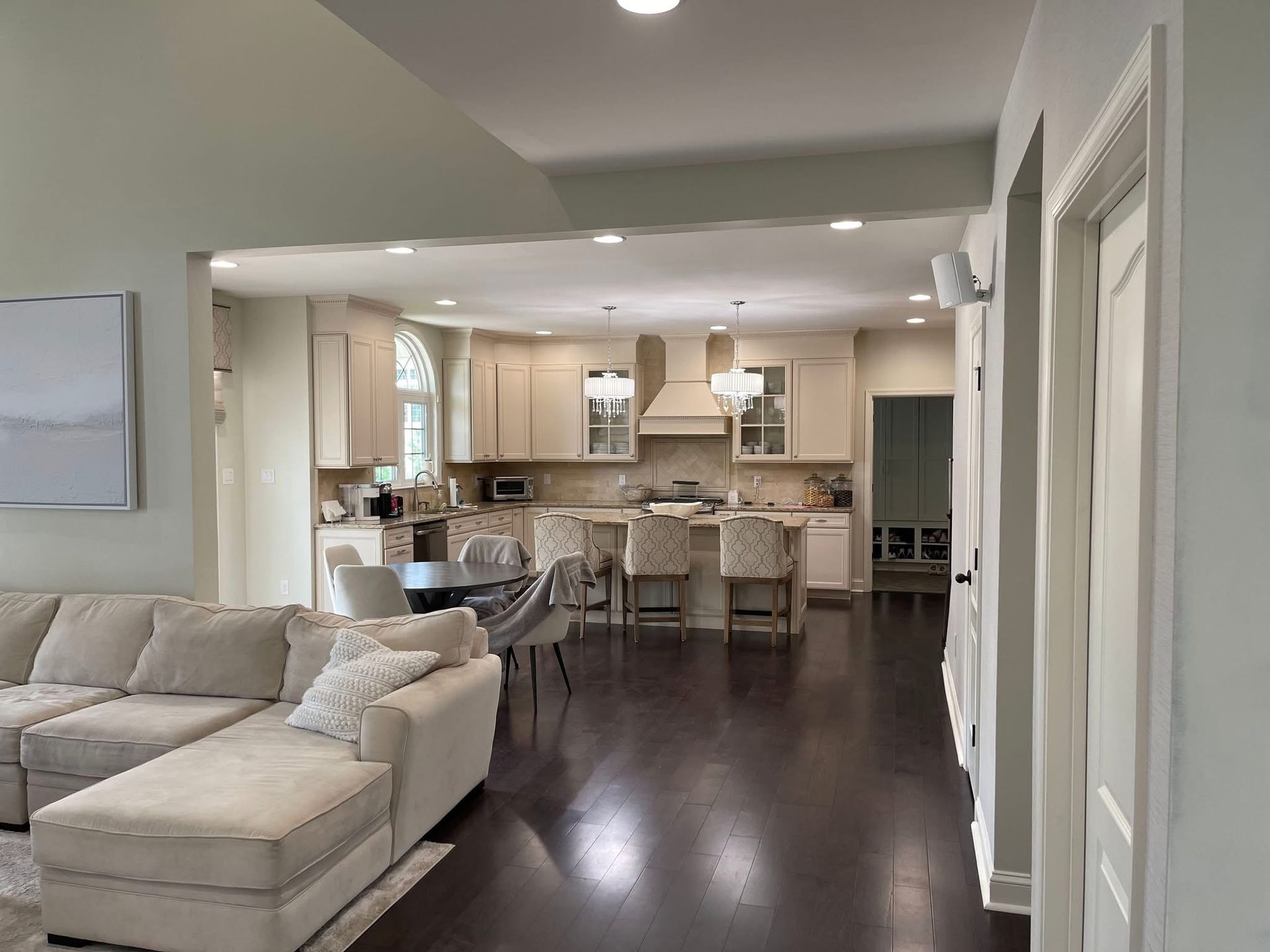 Bright open-concept living room and kitchen with beige sofa, dark wood floors, and bar stools
