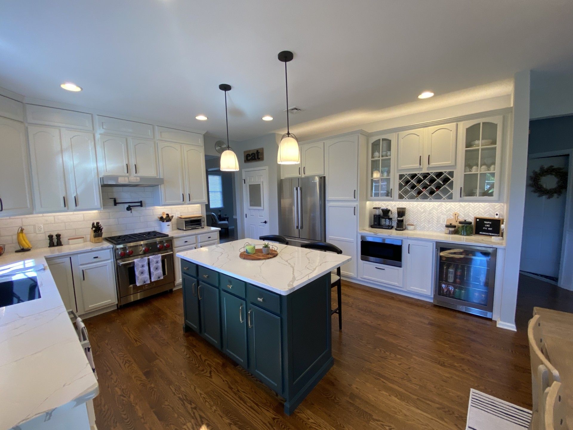 Bright kitchen with white cabinets, teal island, hardwood floors, and pendant lights under recessed ceiling lights