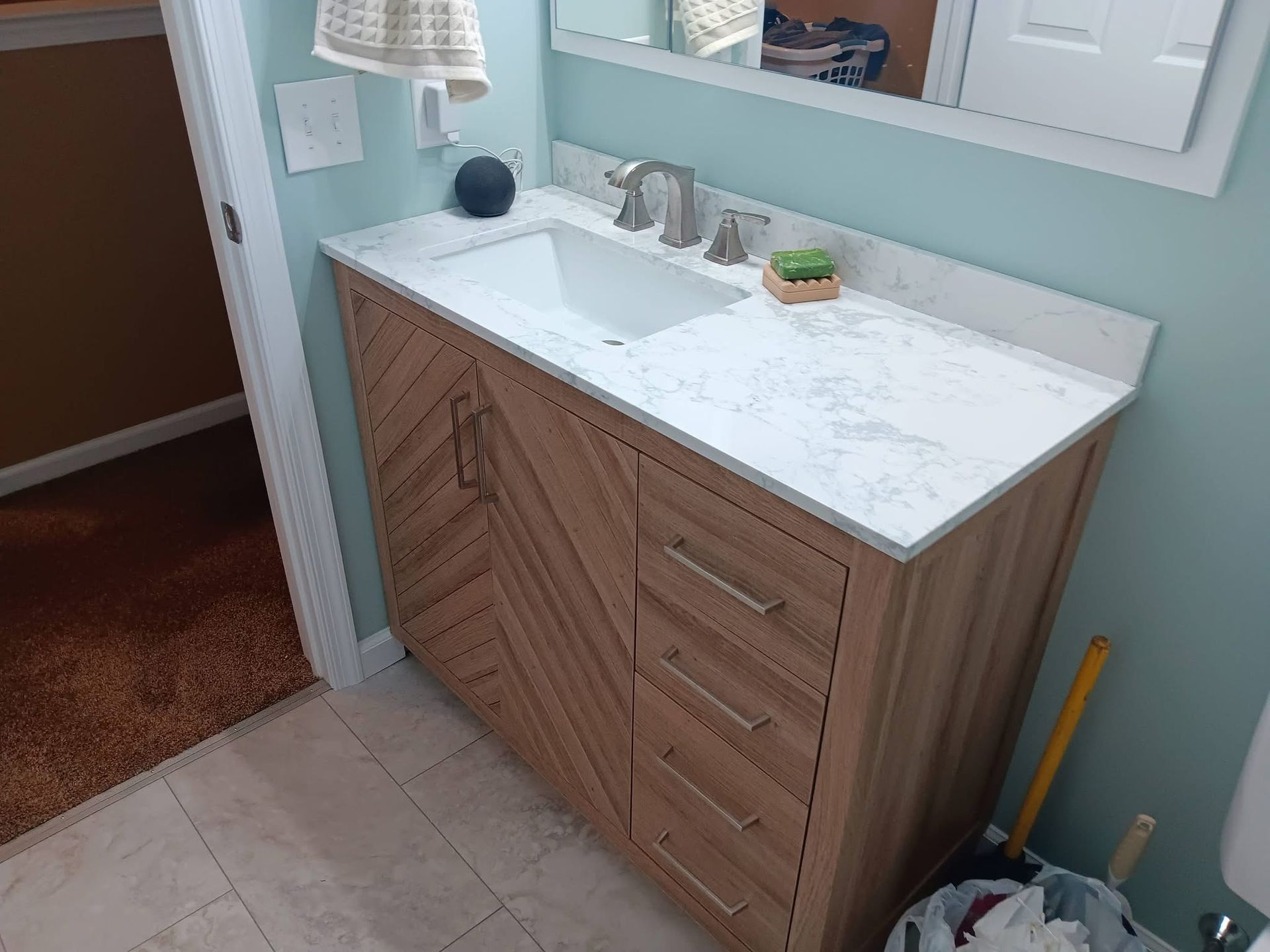 Bathroom vanity with white countertop and wood cabinets beside a sink and mirror.