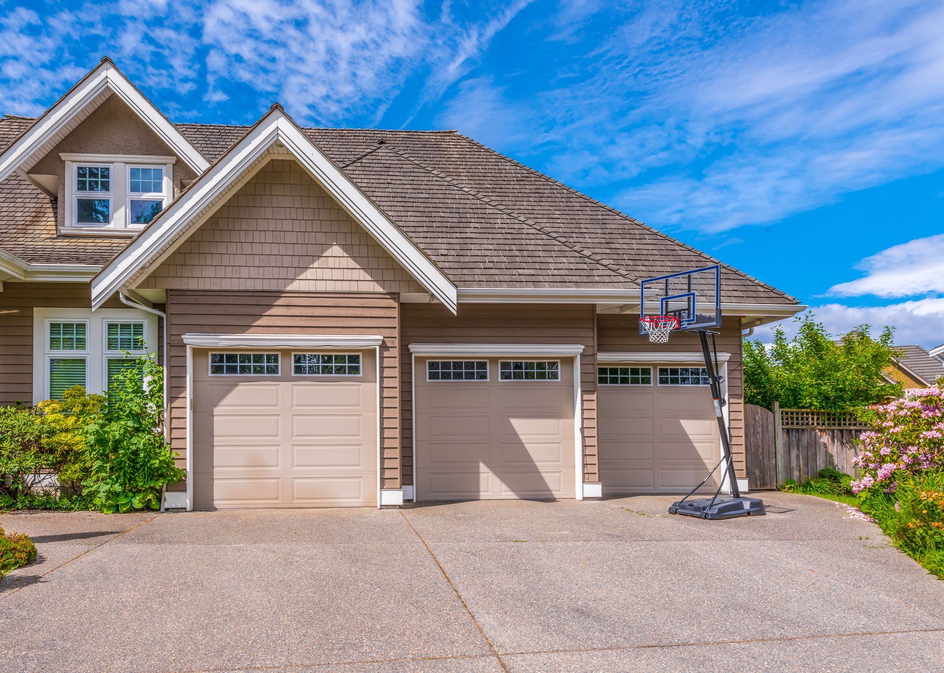 Suburban house with two garage doors, beige siding, and a basketball hoop in the driveway.