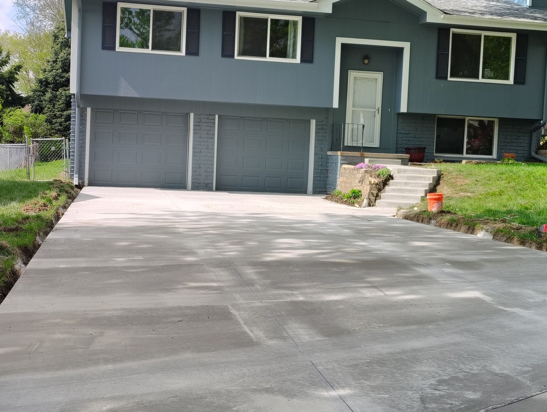 Freshly poured concrete driveway leading to a gray house with double garage doors and a front entrance.