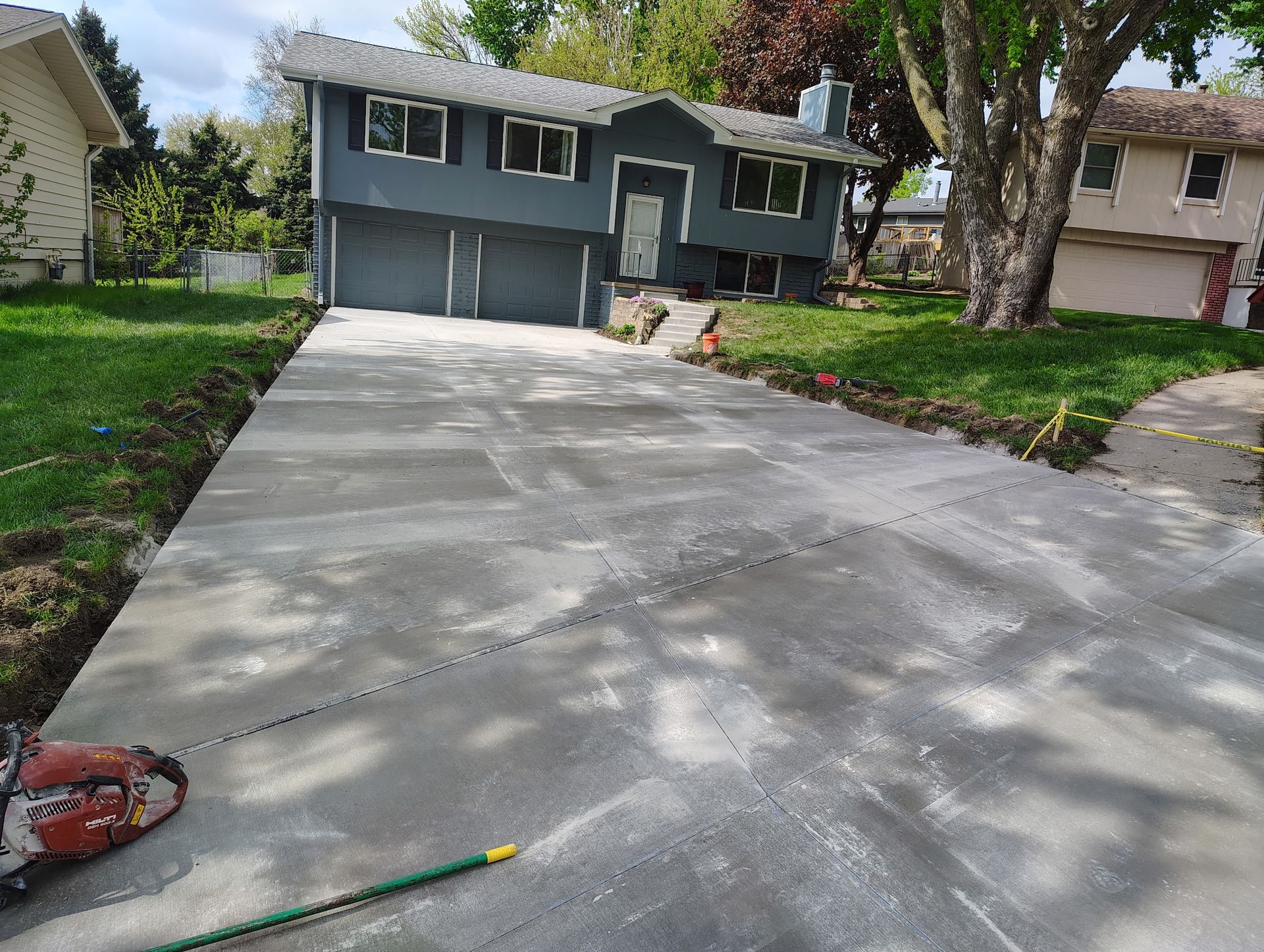 Freshly poured concrete driveway leading to a gray house with a garage and trees casting shadows