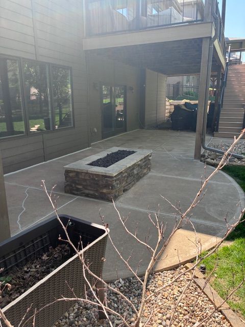 Patio with stone fire pit, covered deck, stairs, windows, and bare branches in the foreground