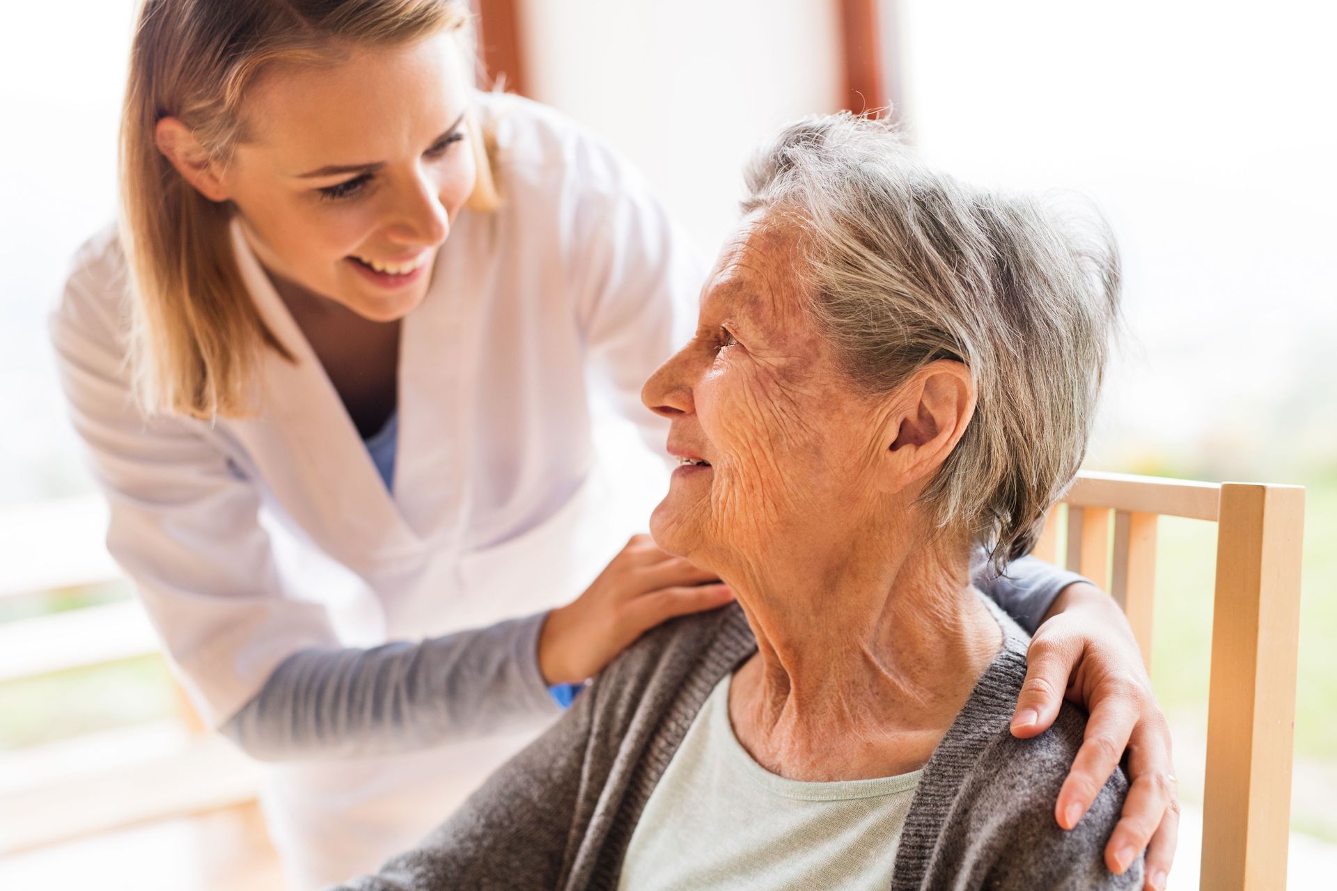 Smiling caregiver with hand on elderly woman's shoulder, indoors.