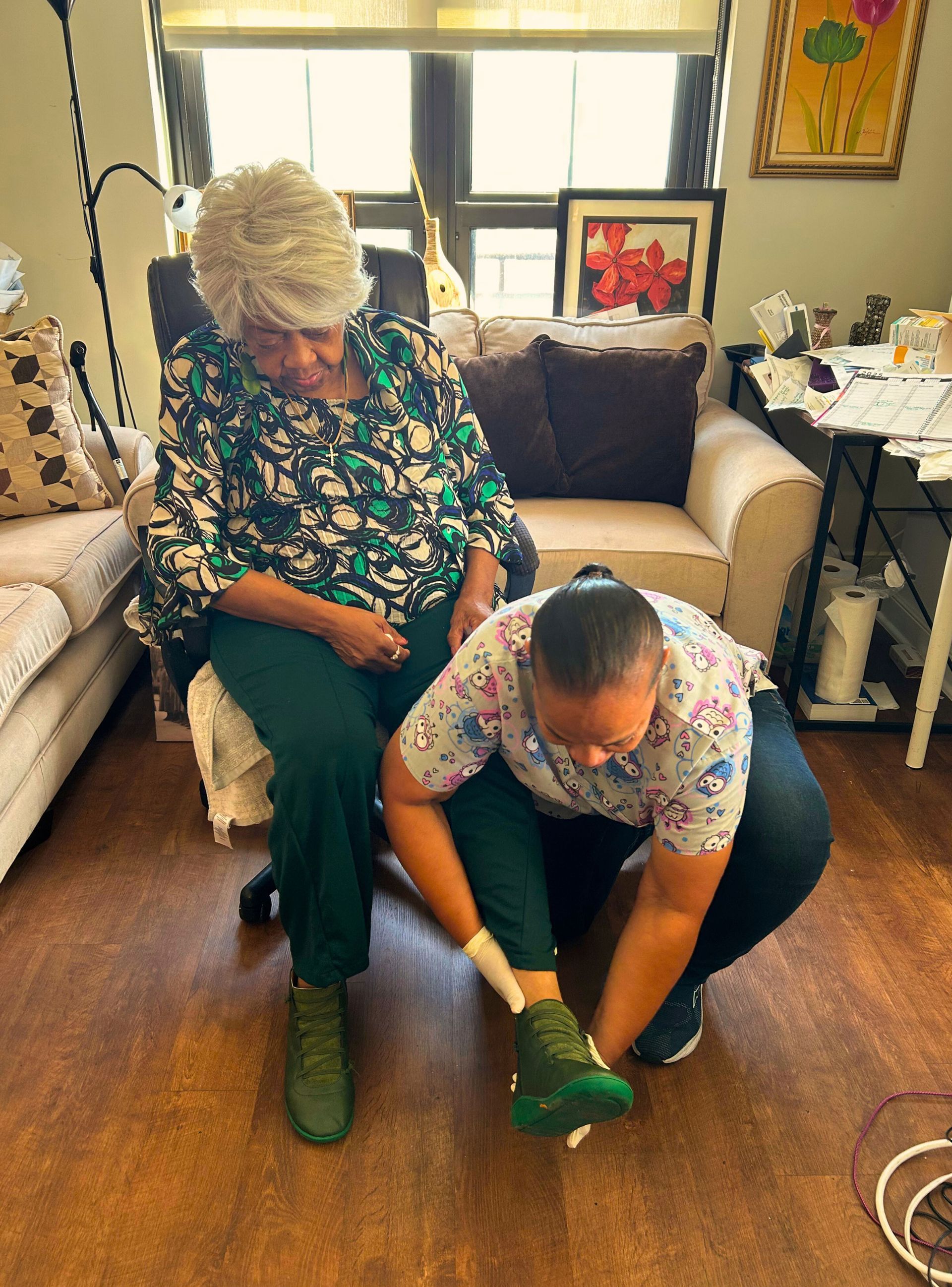 Person seated as another person adjusts their shoe in a room.