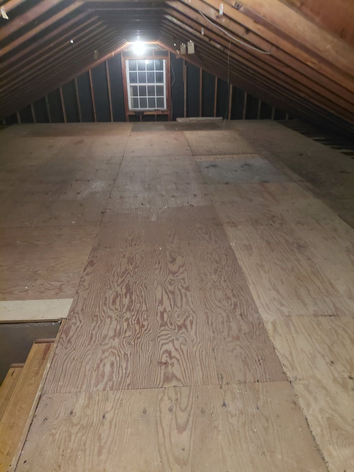 Interior attic with plywood flooring, centered by a small window.