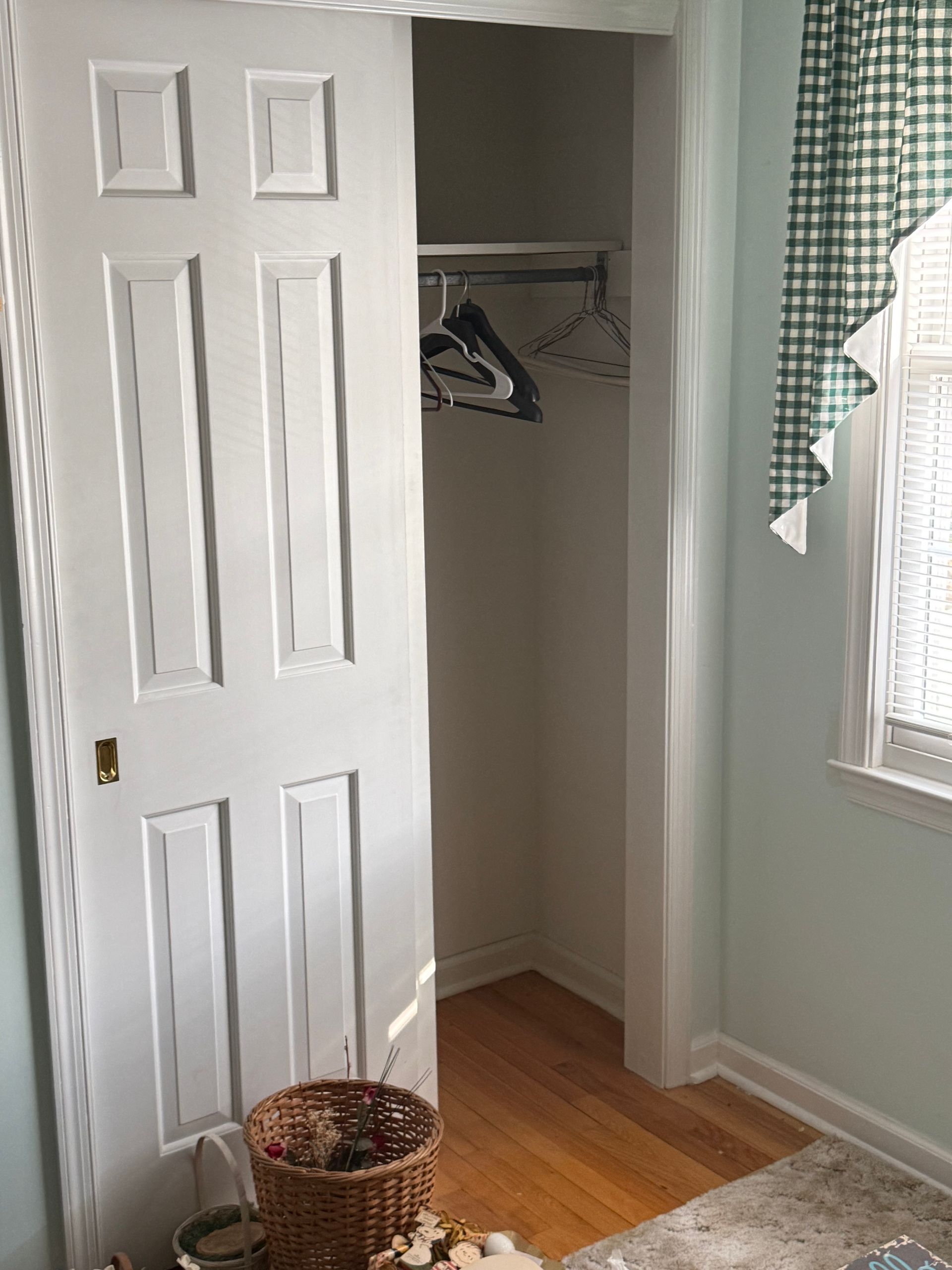 There is a closet with clothes hanging in it and a window.