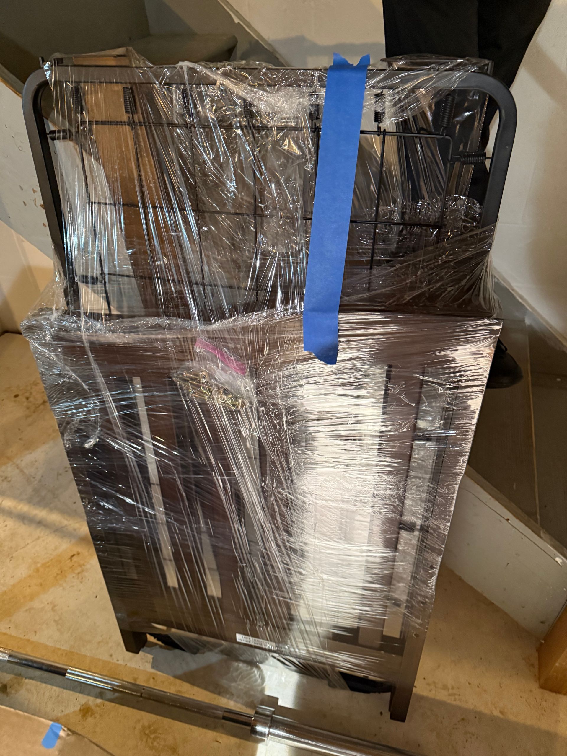 A dishwasher is wrapped in plastic and has a blue tape on it.