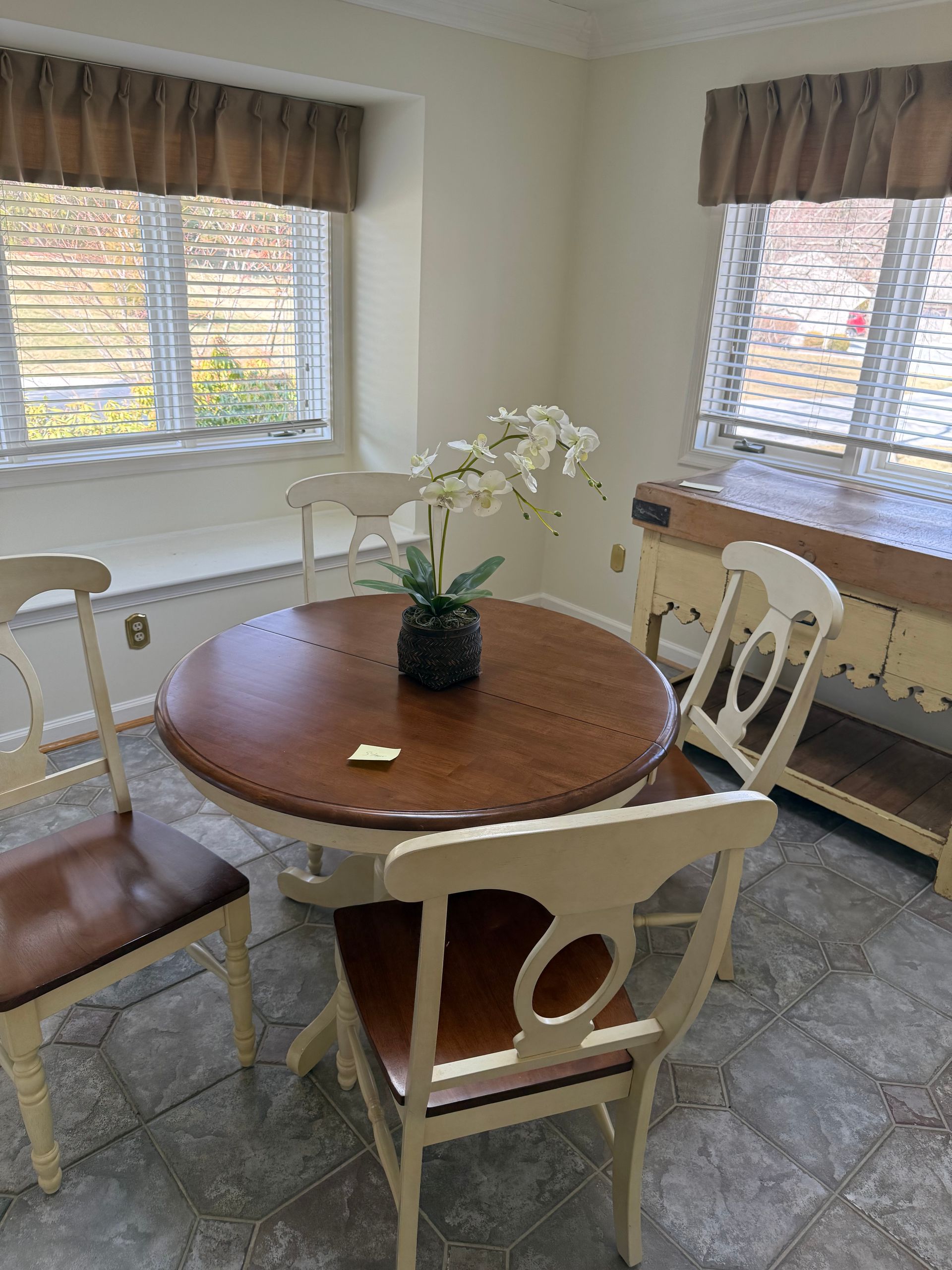 A dining room with a table and chairs and a vase of flowers on the table.