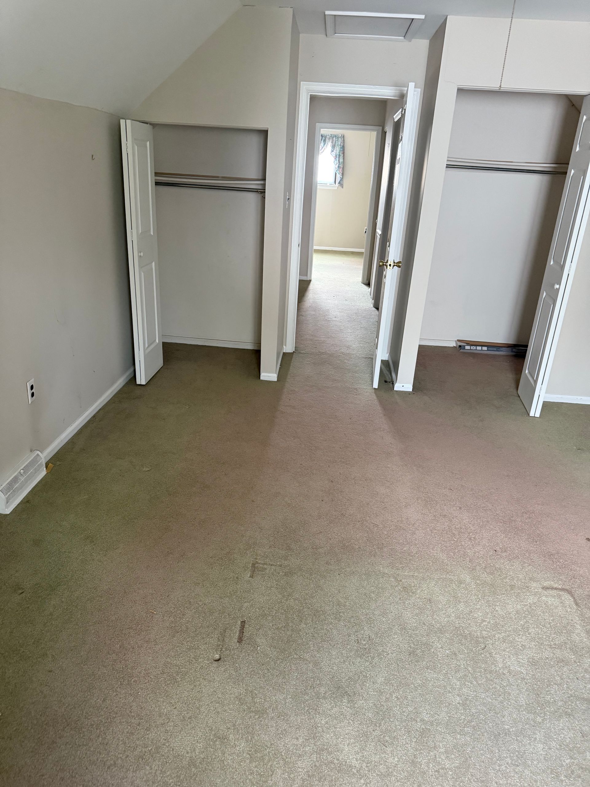 An empty room with a carpeted floor and closets