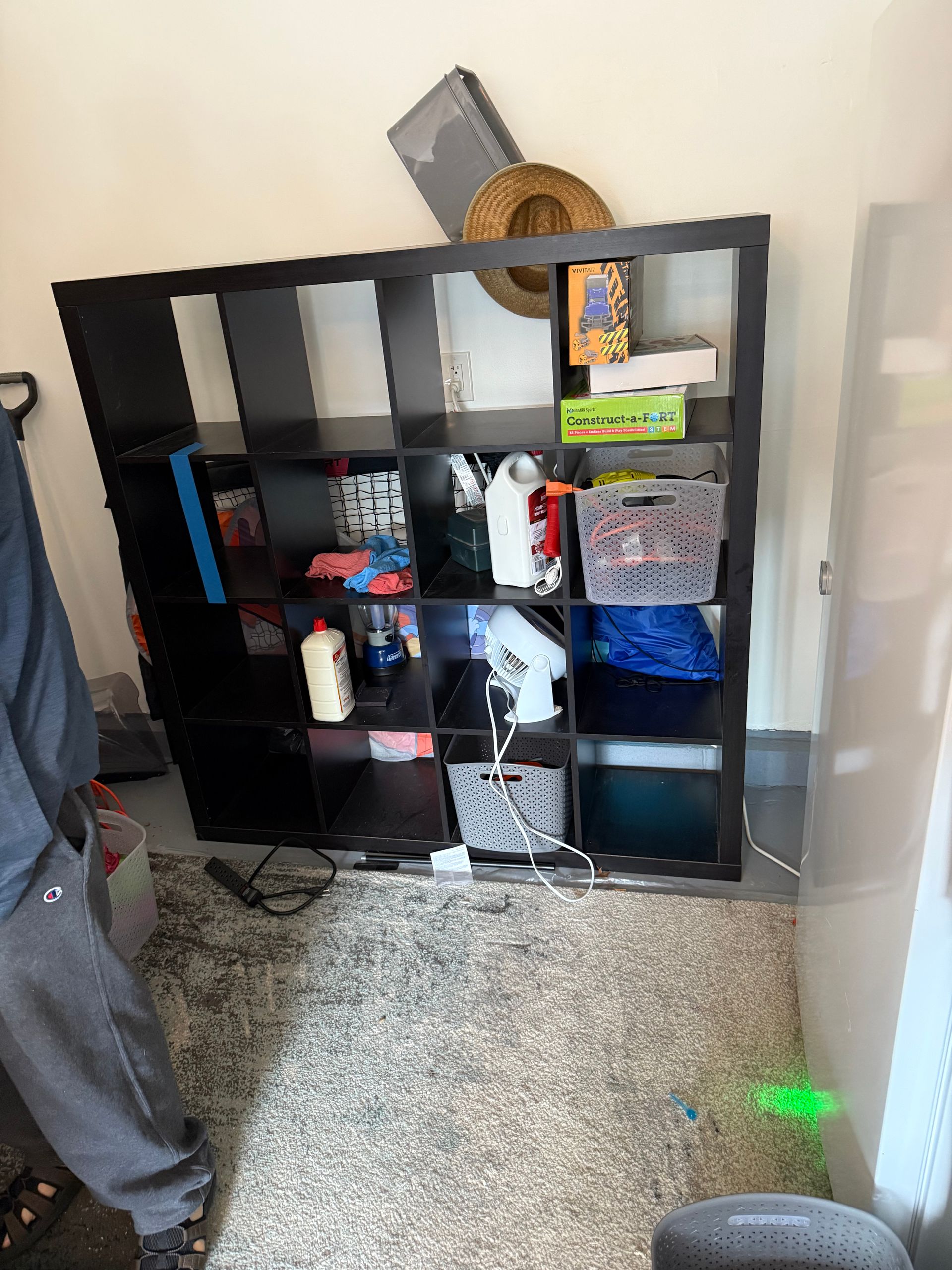 A person is standing in front of a shelf in a room.