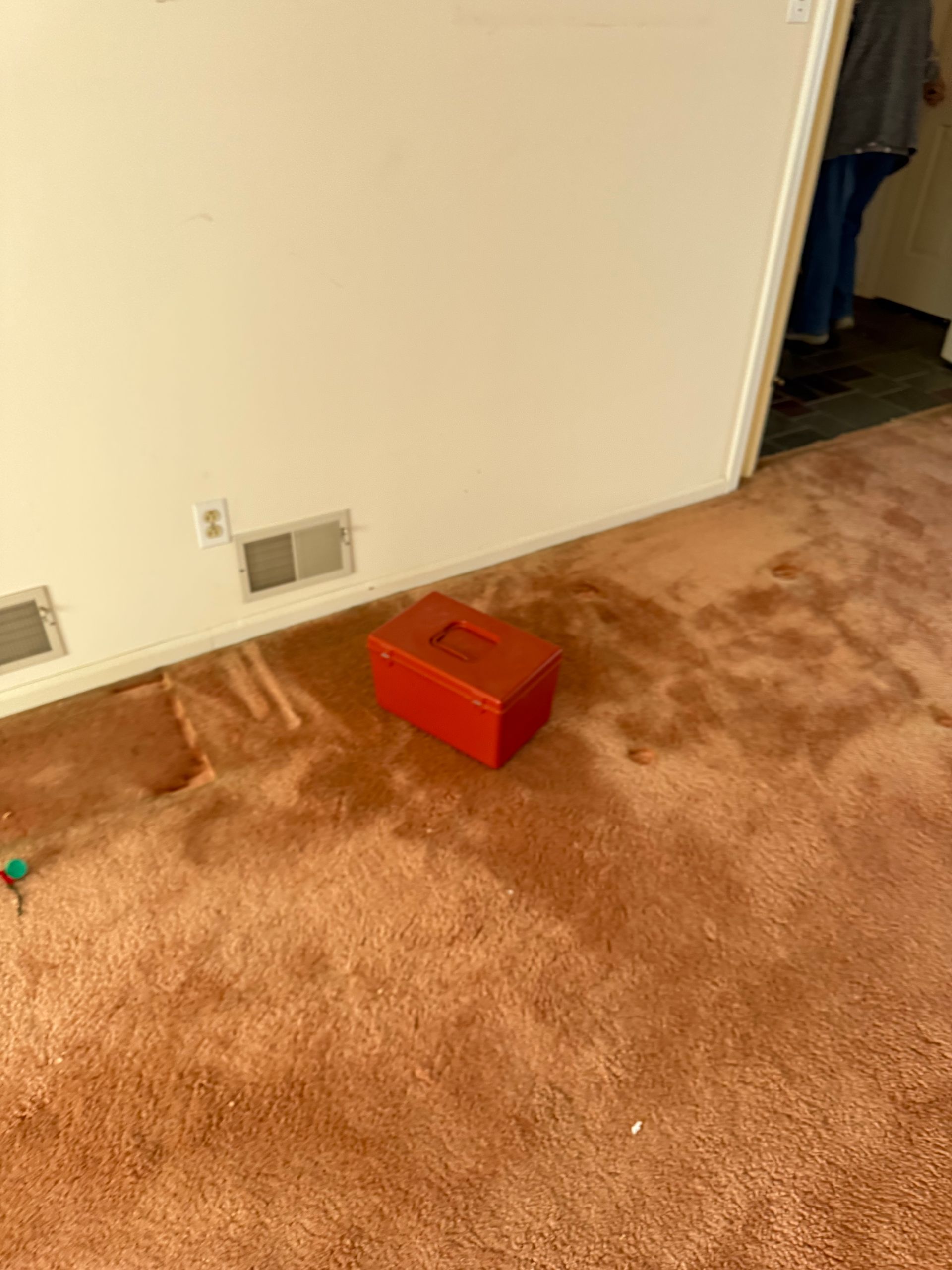 A red box is sitting on a brown carpet in a living room.