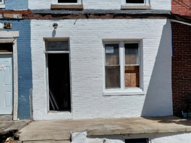 White brick building with open doorway, window, and concrete step.