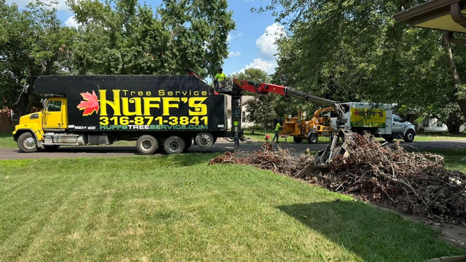 Utility truck with extended crane clearing tree branches on a roadside.