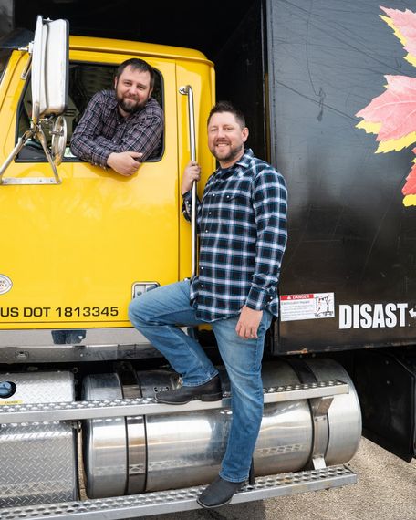 Two smiling people leaning from a bright yellow truck cab door