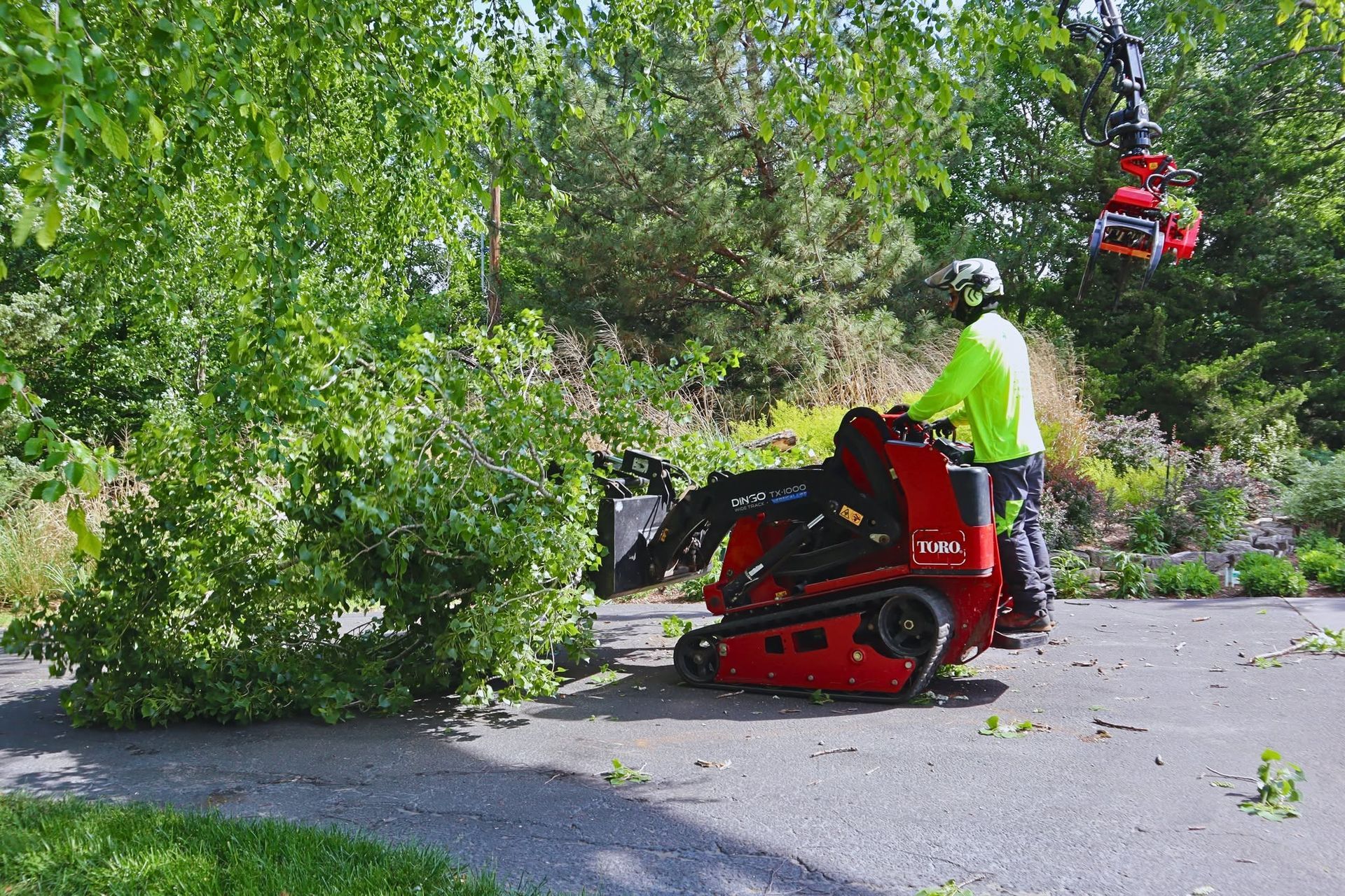 Worker operating a red wood chipper trimming a fallen tree on a leafy roadside