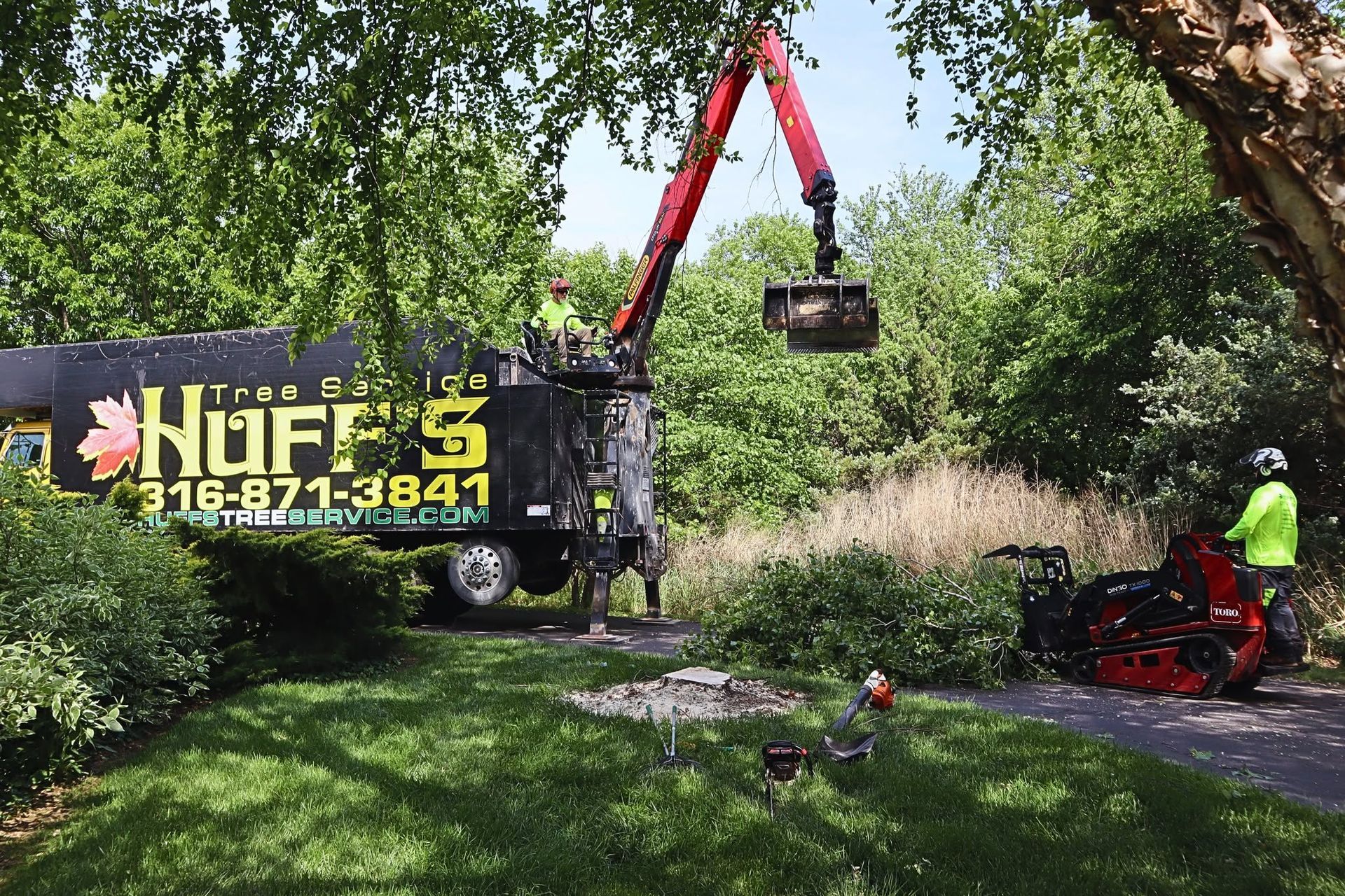 Tree service crew trimming a large tree with a crane truck in a leafy yard