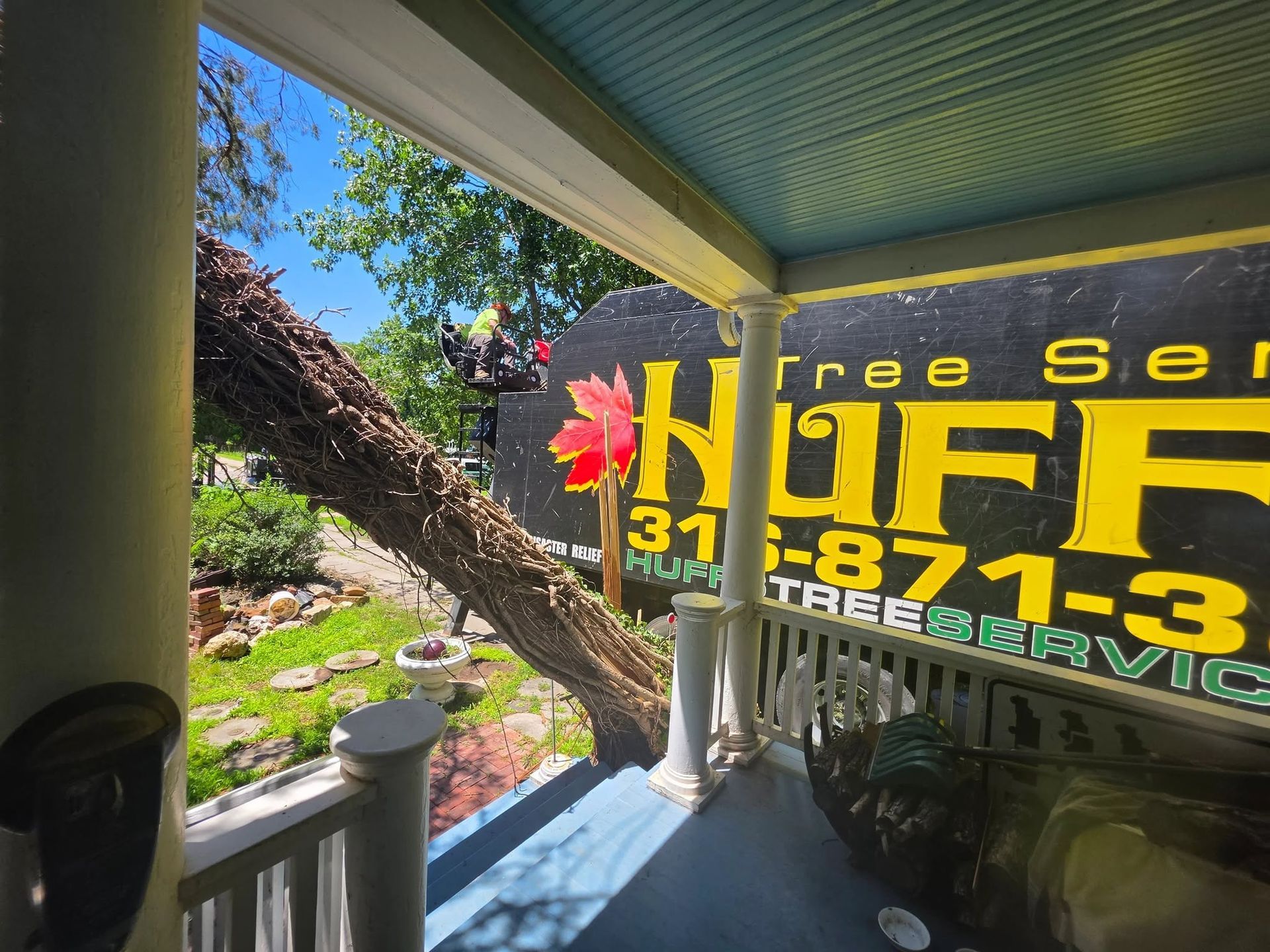 Yellow tree service sign on a porch, with flowers and a sunny garden in the background.