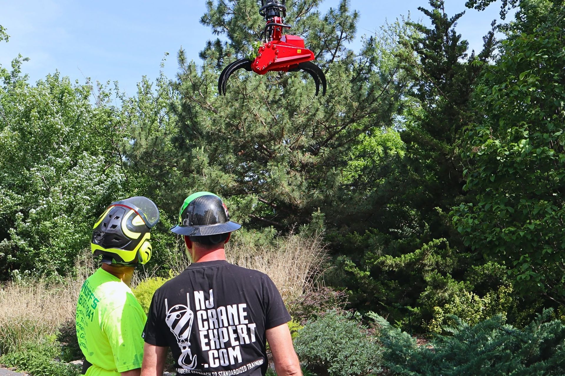 Two workers in helmets watching a red drone above dense green trees