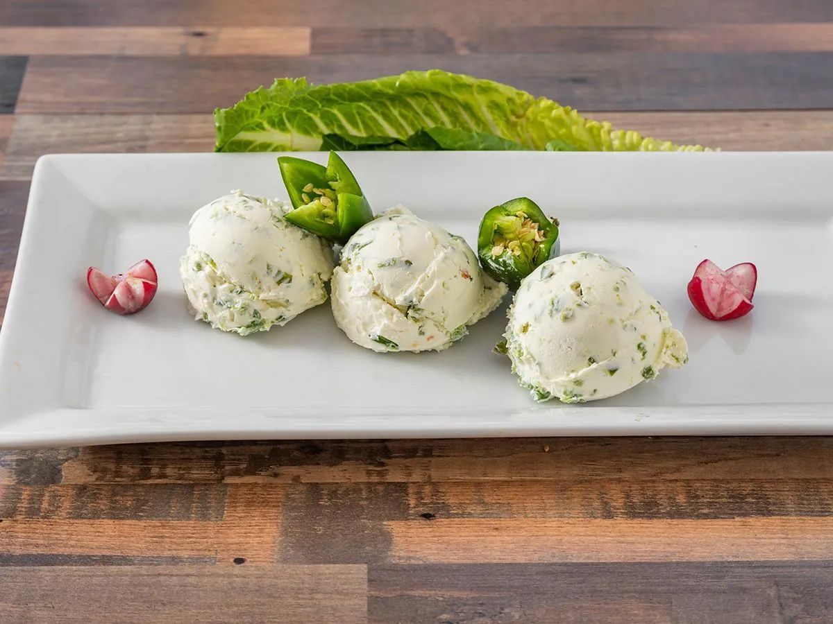 A white plate topped with mashed potatoes and jalapenos on a wooden table.