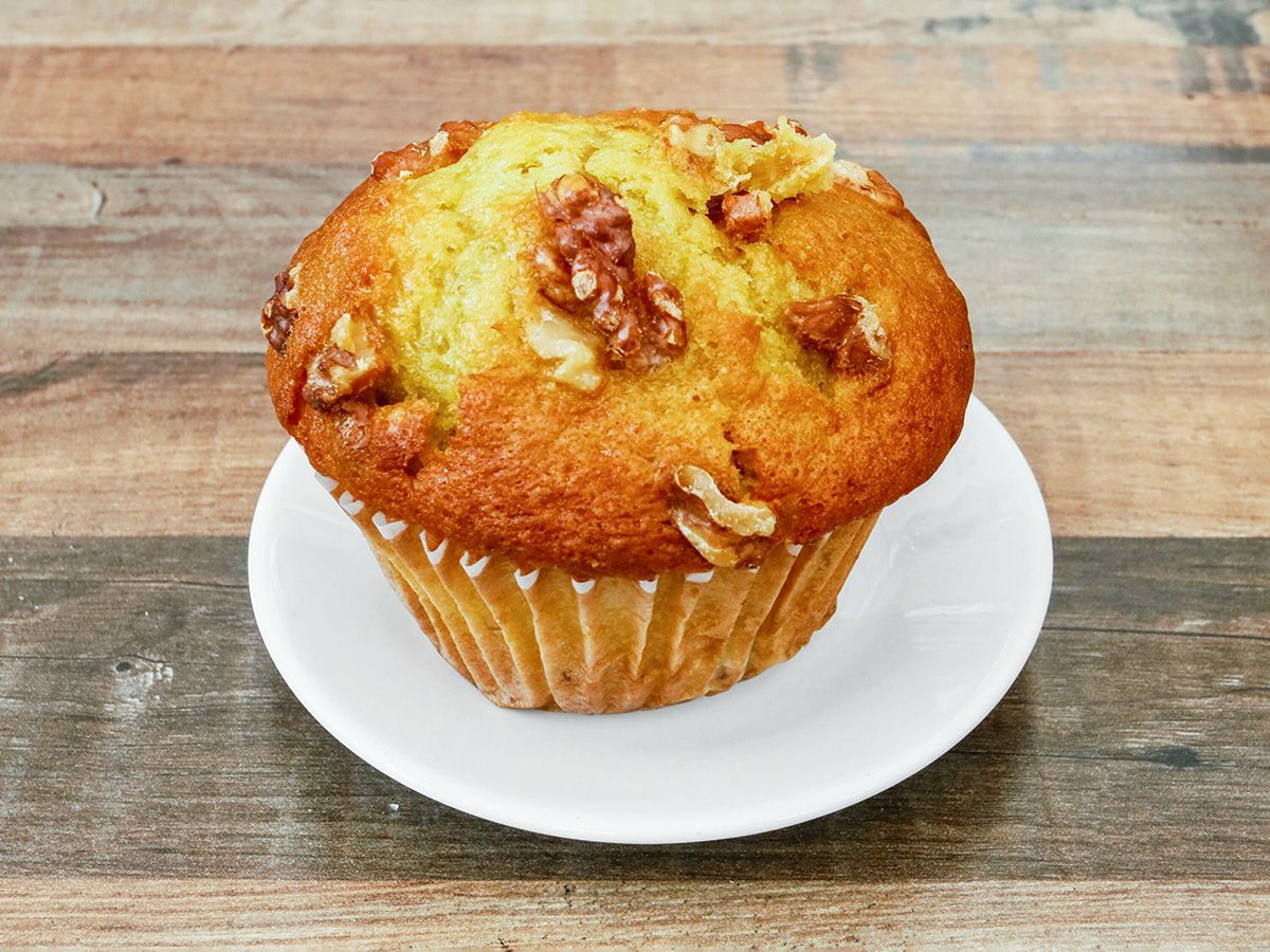 A cupcake with walnuts on top is on a white plate on a wooden table.