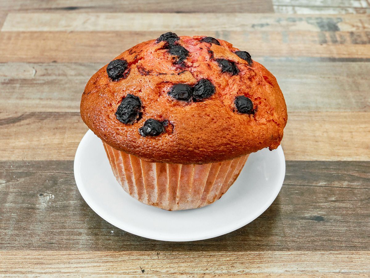 A cupcake with blueberries on top is on a white plate on a wooden table.