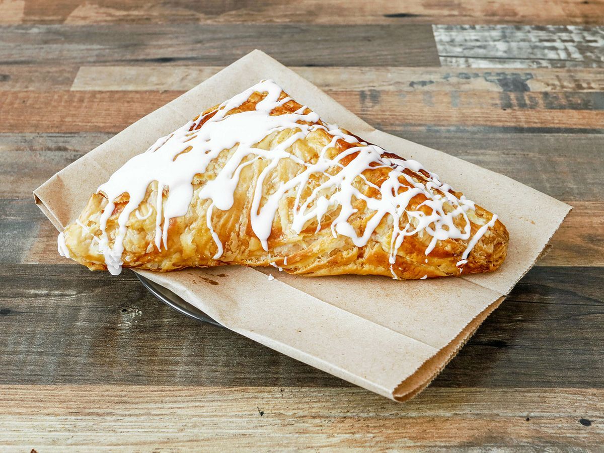 A pastry is sitting on a piece of paper on a wooden table.