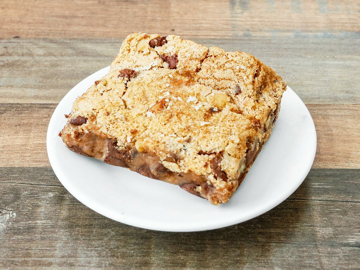 A cookie bar is on a white plate on a wooden table.