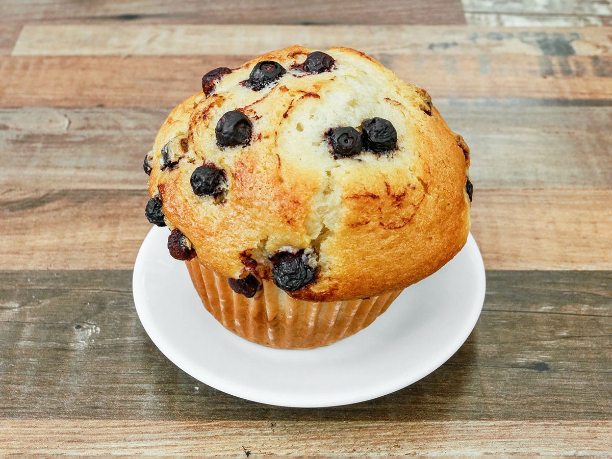 A blueberry muffin is on a white plate on a wooden table.