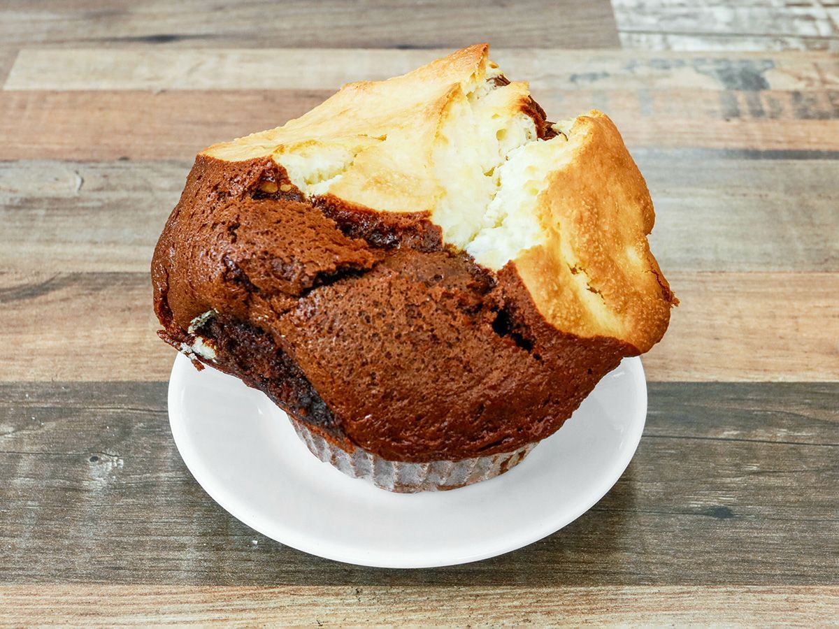 A muffin with a bite taken out of it is on a white plate on a wooden table.