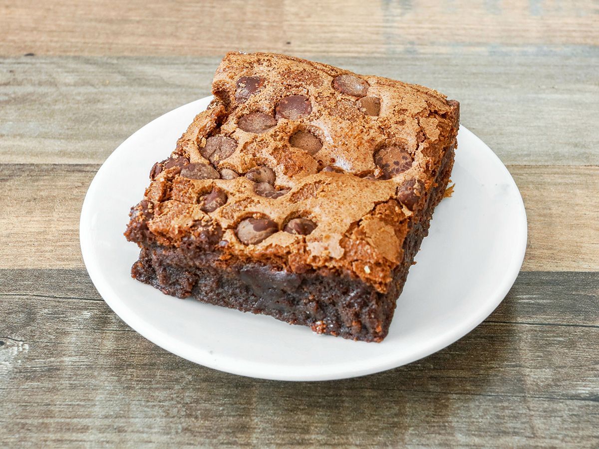 A brownie with chocolate chips on a white plate on a wooden table.