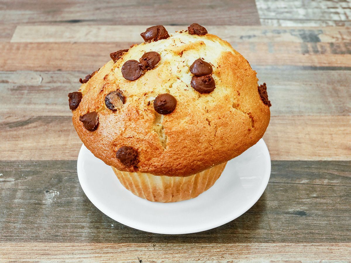 A muffin with chocolate chips on a white plate on a wooden table.