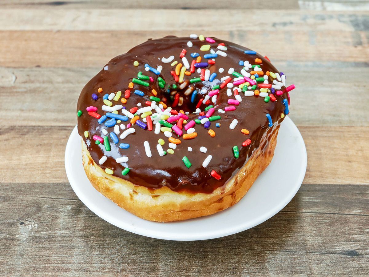 A chocolate donut with sprinkles on a white plate on a wooden table.