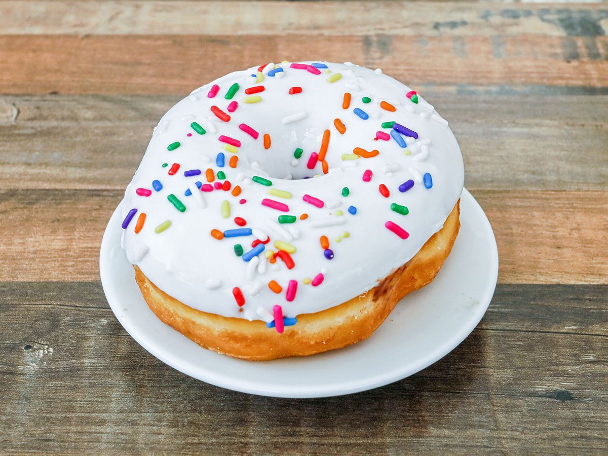 A white donut with sprinkles on a white plate on a wooden table.