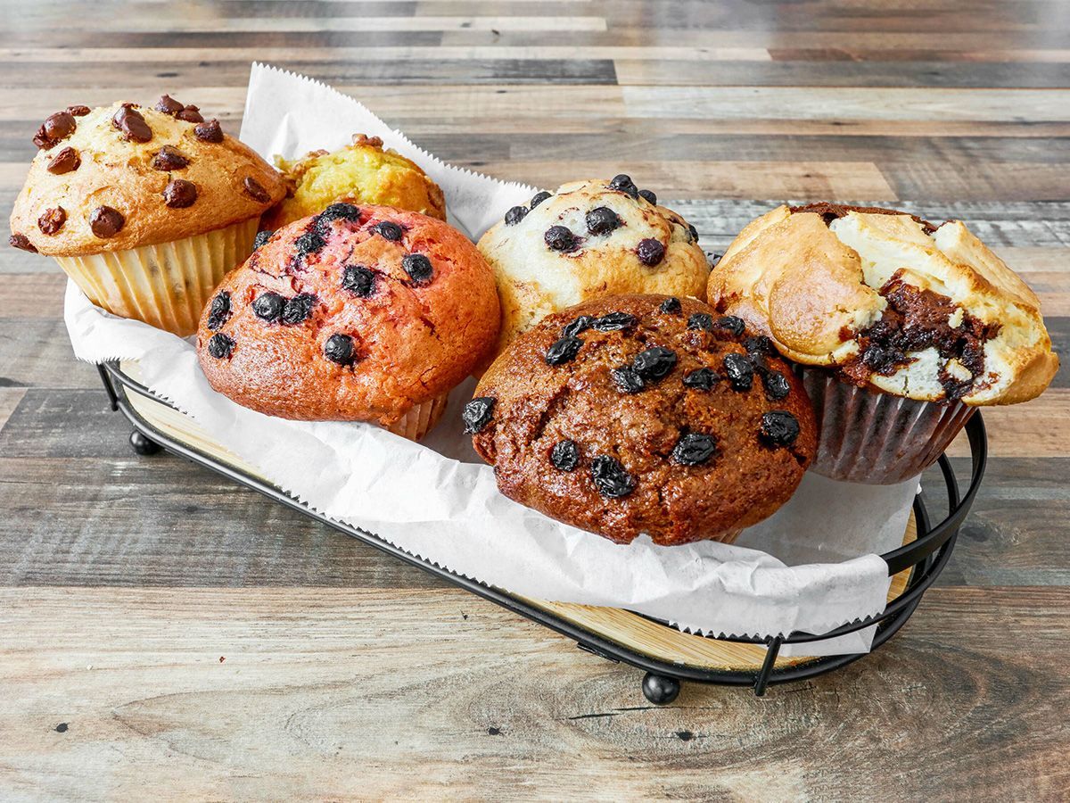 A basket filled with a variety of muffins on a wooden table.