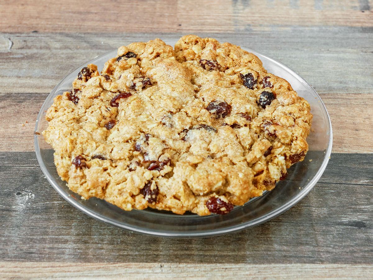 An oatmeal cookie with raisins on a glass plate on a wooden table.